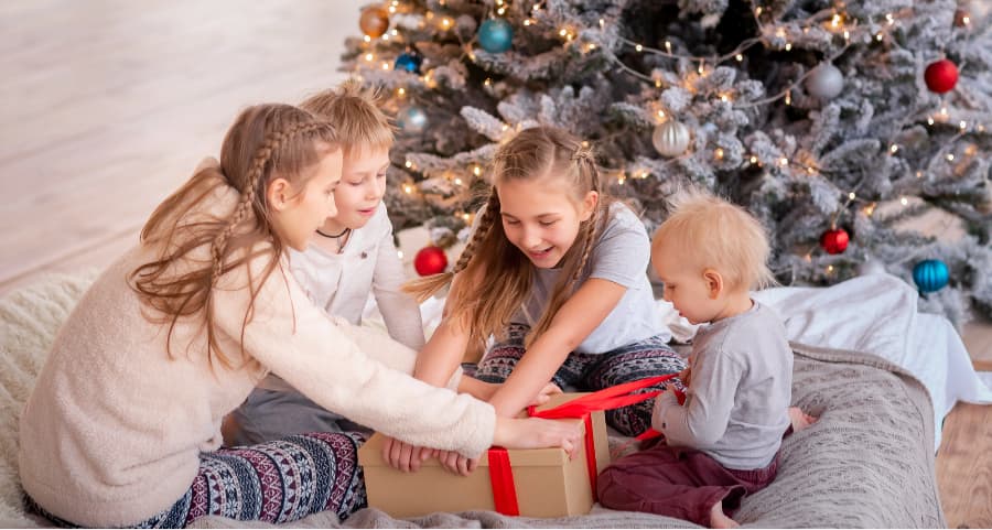 Kids opening a present in the family room beside a Christmas tree.
